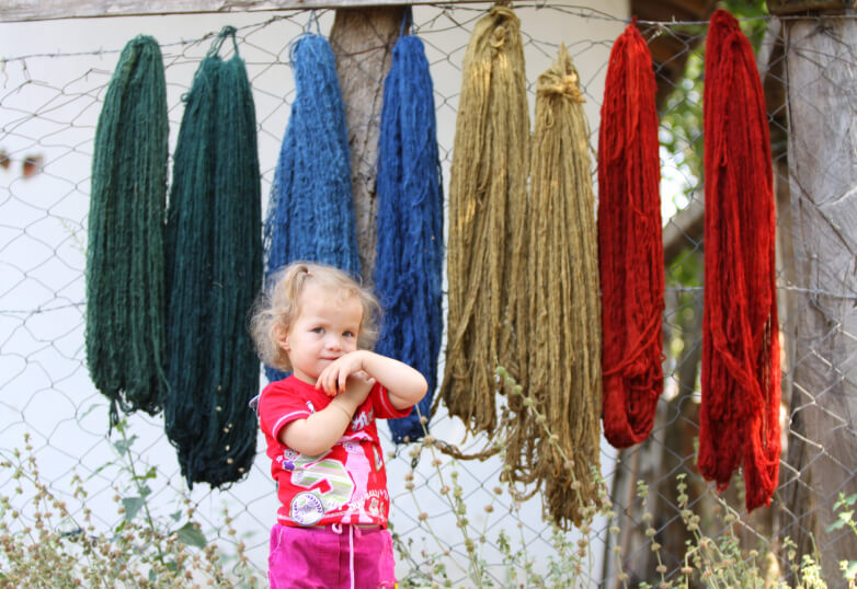 草木染めされ干してある糸の前にいる女の子の写真