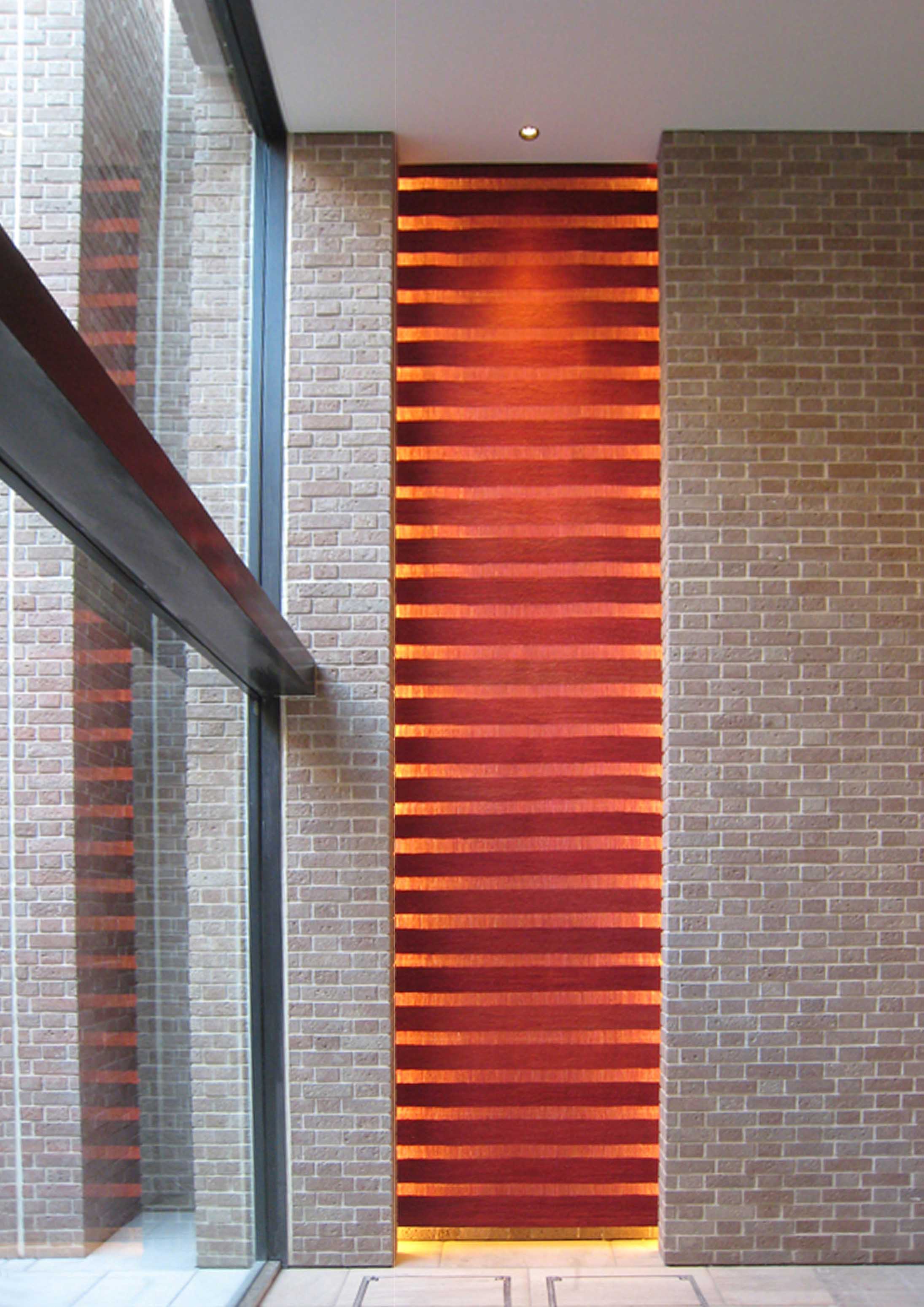 背後の照明が点灯されたスエントランスホールに飾られる赤いSUKASI KILIMの正面からの写真